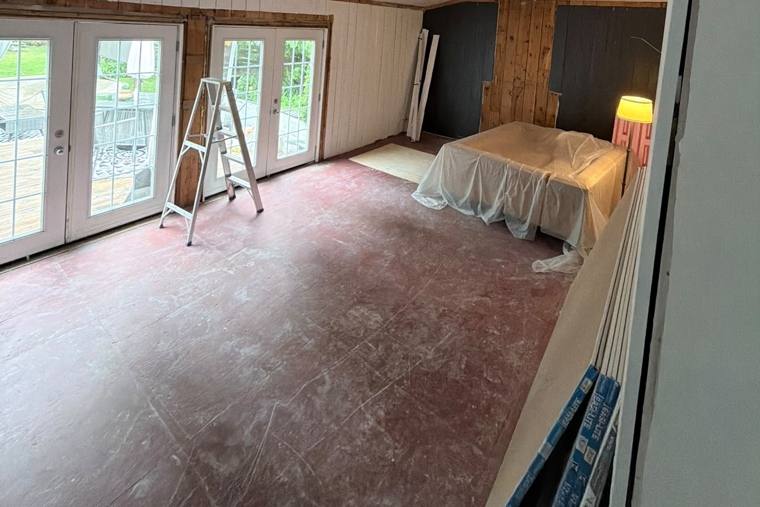 Gutted sunroom addition with red painted subfloor and French doors