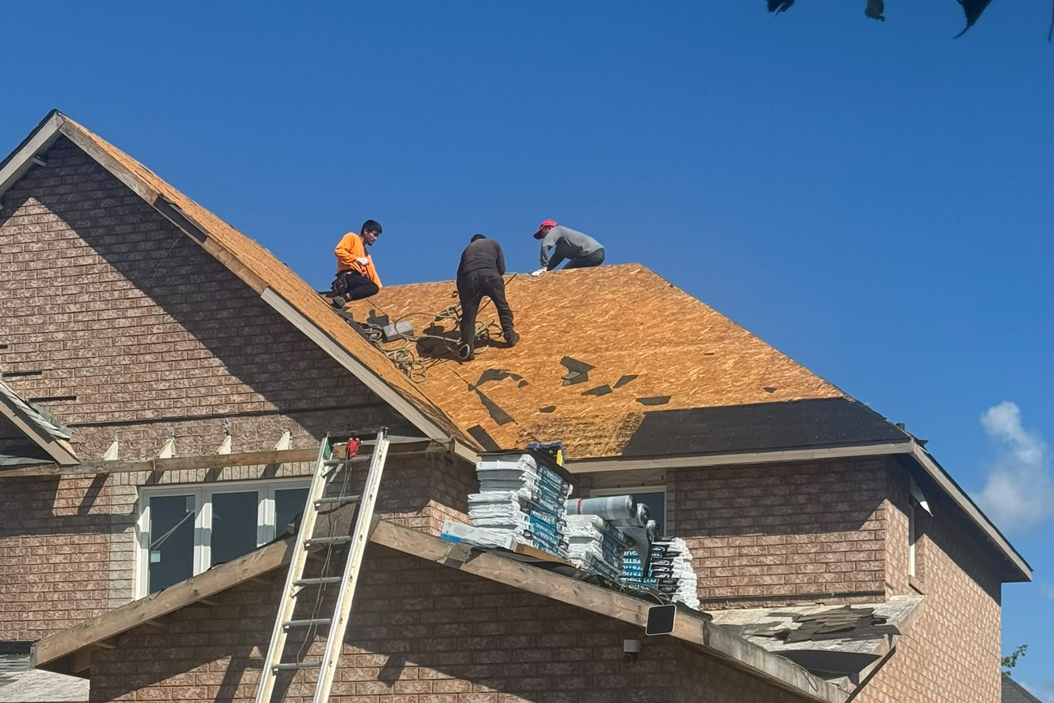 Roof mid-tear-off with plywood decking and workers installing shingles